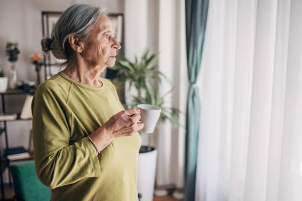 istock Elderly woman  at home drinking coffee and looking through the window 1440736876