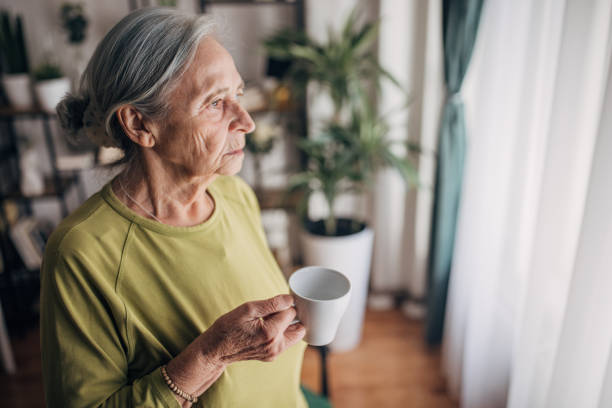 istock Elderly woman  at home drinking coffee and looking through the window 1440736956