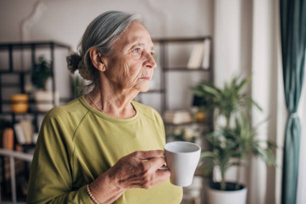 istock Elderly woman  at home drinking coffee and looking through the window 1440736986