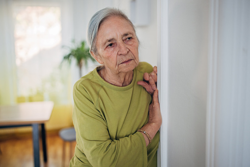 Elderly woman  looking through the window at home