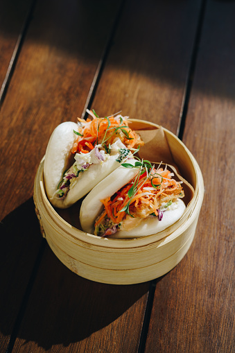 Steamed bao buns with vegetables in a bamboo dish on a wooden table