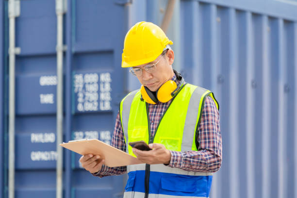 istock Engineer with clipboard checklist in industry containers cargo, Foreman dock worker in hardhat and safety vest control loading containers box from cargo 1440745774