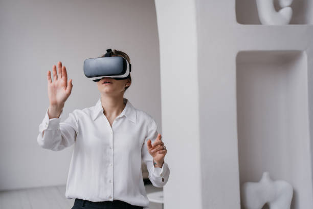 istock Young female student in white shirt and black pants using vr glasses exploring arts and museums standing indoors against wall with ceramics  on shelves. Girl using virtual reality. Education and fun. 1440745978