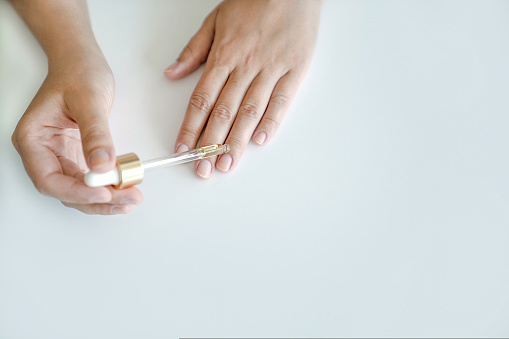 Cuidado de la piel de uñas y manos. La mujer sostiene una pipeta con aceite para aplicar a sus uñas para el tratamiento y fortalecimiento de las uñas. Manos en primer plano, espacio de copia photo