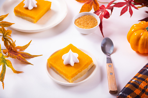 Slice of fresh baked traditional American homemade pumpkin pie cut into square pieces decorating whipped cream for celebrating holidays