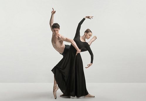 Young man and woman, ballet dancers performing isolated over grey studio background. Wonderful synergy. Concept of classical dance aesthetics, choreography, art, beauty. Copy space for ad