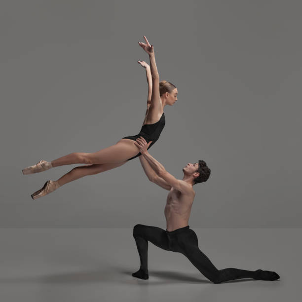 giovane uomo e donna, ballerini che si esibiscono isolati su uno sfondo grigio scuro dello studio. bella coppia tenera - ballerino in punta di piedi foto e immagini stock