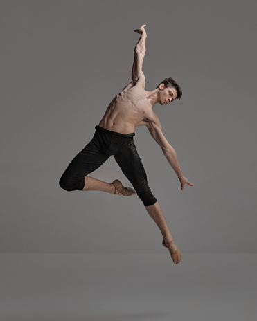 Portrait of young muscular man, ballet dancer performing isolated over dark grey background. Expressing freedom. Concept of classical dance aesthetics, choreography, art, beauty. Copy space for ad