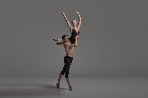 Young man and woman, ballet dancers performing isolated on dark grey studio background. Keeping balance on shoulder. Concept of classical dance aesthetics, choreography, art, beauty. Copy space for ad