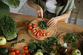 High angle view of hands of woman chopping arugula leaves, sitting at table in bright exotic studio