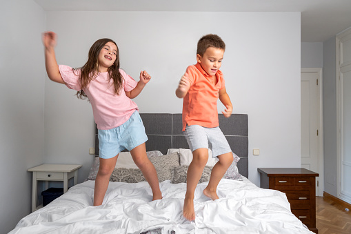 Playful siblings jumping on the bed. High quality photography.