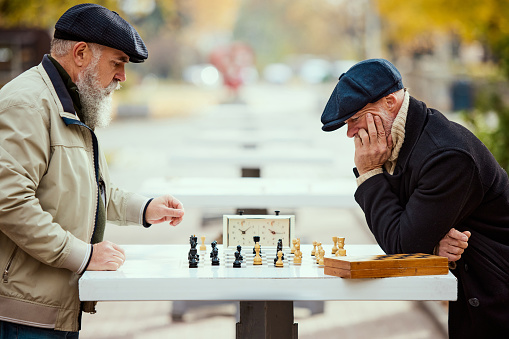 Portrait of two senior men playing chess in the park on a daytime in fall. Thoughtful activity. Concept of leisure activity, friendship, sport, autumn season, game, entertainment, old generation