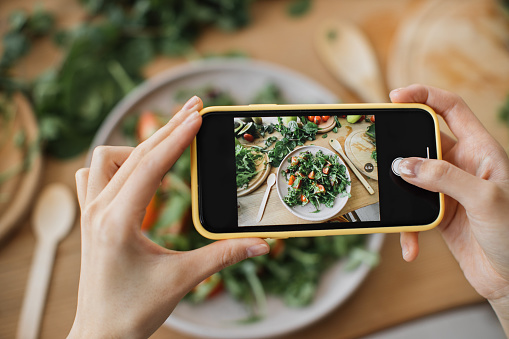 Woman hands take phone photo of food lunch or dinner. Vegetable salad, avocado, arugula tomatoes. Smartphone photography for social networks. Raw vegan vegetarian healthy food.