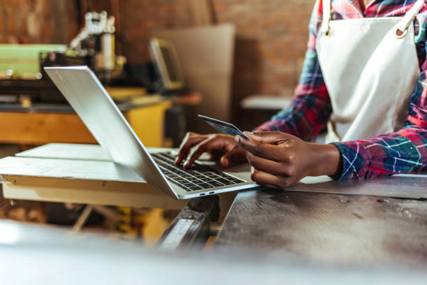 istock Carpenter at work holding a credit card and typing on a laptop. 1440753046