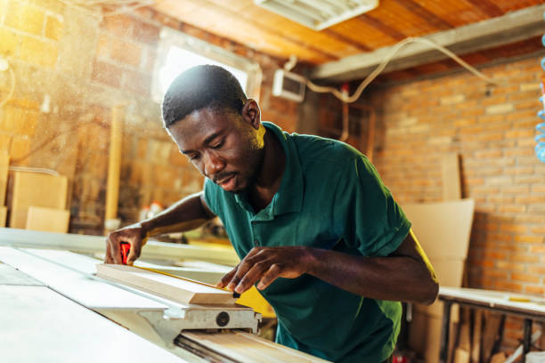 istock Young man carpenter on building site measuring with tape measure 1440754355