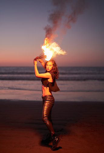 young latin female fire perfomer holding fire fans above her head on the beach at night