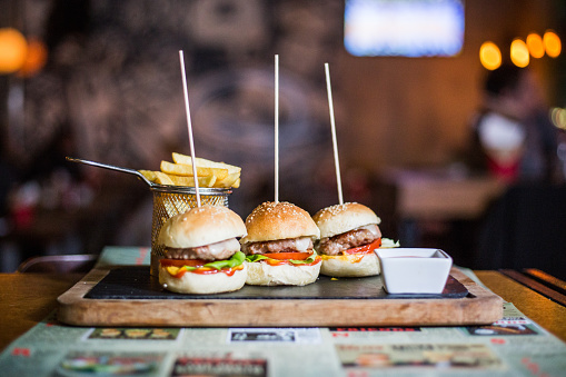 A closeup shot of three mini burgers with french fries and sauce on a wooden tray - food blog concept