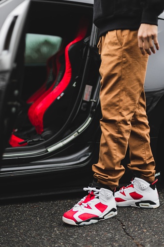 charlotte, United States – August 05, 2022: A vertical shot of a male wearing red Jordan 6 carmine sneakers with a car in the background