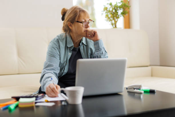istock Active mature woman using a laptop for remote work from the home office. Video conference, video meeting. Senior teacher leads webinar 1440761516