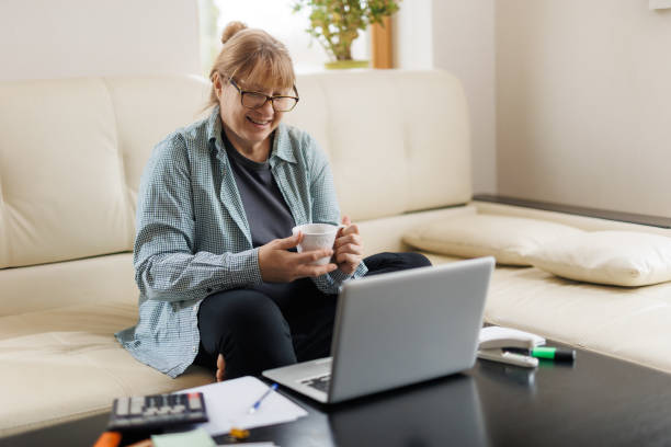 istock Serene mature female with blond hair having hot tea or coffee while working remotely in front of laptop at home 1440761598