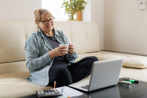 istock Serene mature female with blond hair having hot tea or coffee while working remotely in front of laptop at home 1440761600