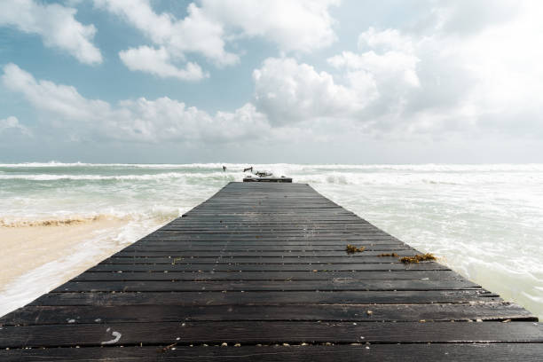 Beautiful shot of a wooden road to the ocean or to the sea coast under a cloudy sky A beautiful shot of a wooden road to the ocean or to the sea coast under a cloudy sky ebb and flow stock pictures, royalty-free photos & images