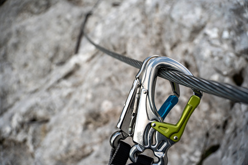 Via ferrata set with colorful carabiners hangs on a wire rope on a rocky mountain.