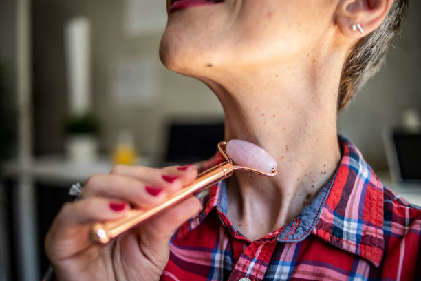 a mature woman with short hair is massaging her face with a derma roller while sitting in her workspace in the apartment - looking glass rock imagens e fotografias de stock