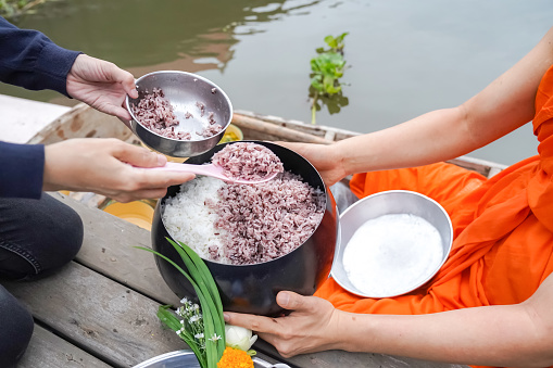 The monk was Holding monk's alms-bowl, between Thai Local people make merit by offering food rice to the monk who in a vintage wooden boat in the morning.