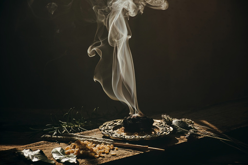 Charcoal burning with incense, incense resin, rosemary, 
laurel, lavender on a rustic wooden table, 
smudge stick, smudging, energetic cleansing and s