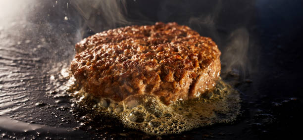 Thick juicy minced beef patty for a traditional burger grilling on a griddle