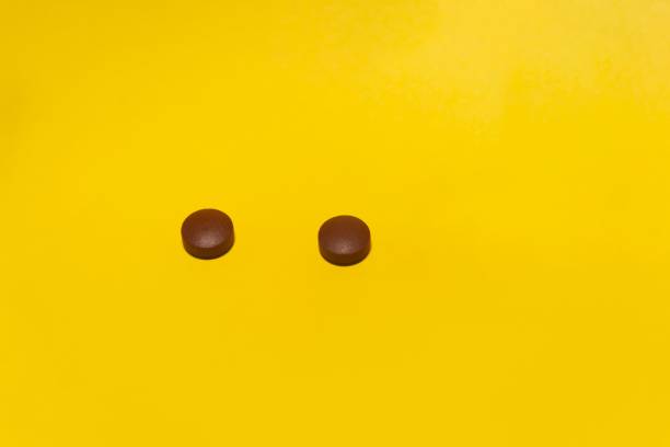 istock Close-up shot two brown pills isolated on yellow background 1440763557