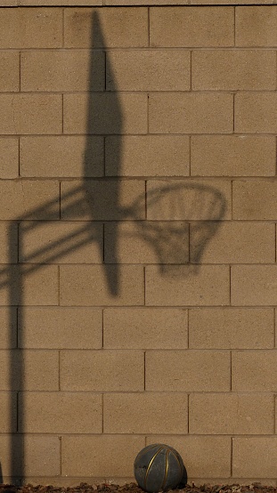 A vertical closeup of a sunlit brick wall with basketball backboard shadow on it