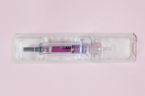 Individually sealed syringe pre-filled with a medical solution in a plastic blister on a textured pink paper background. Science health and medicine.