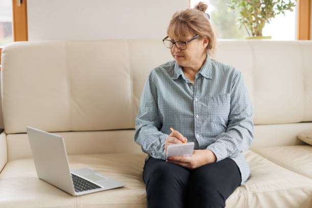 istock Active mature woman using a laptop for remote work from the home office. Video conference, video meeting. Senior teacher leads webinar 1440765759