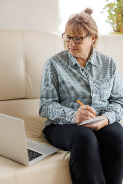 istock Active mature woman using a laptop for remote work from the home office. Video conference, video meeting. Senior teacher leads webinar 1440765968