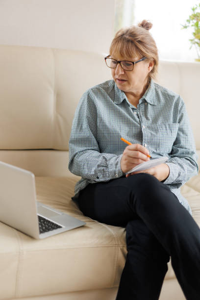 istock Active mature woman using a laptop for remote work from the home office. Video conference, video meeting. Senior teacher leads webinar 1440765986
