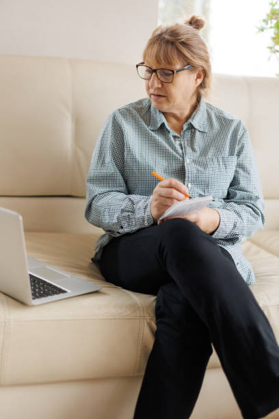 istock Active mature woman using a laptop for remote work from the home office. Video conference, video meeting. Senior teacher leads webinar 1440765989