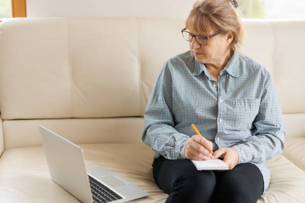 istock Active mature woman using a laptop for remote work from the home office. Video conference, video meeting. Senior teacher leads webinar 1440766005
