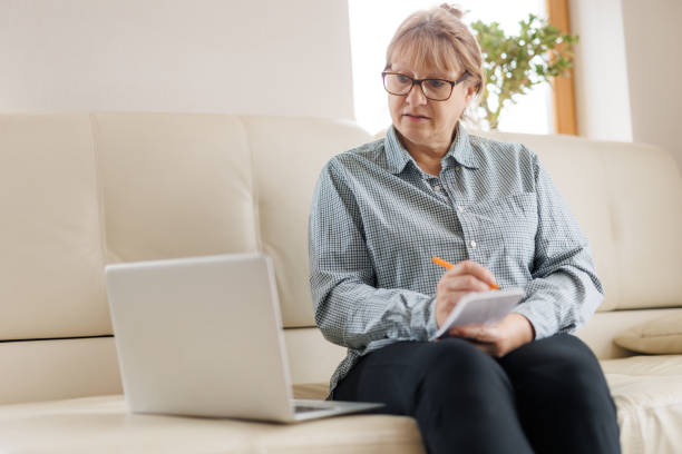 istock Active mature woman using a laptop for remote work from the home office. Video conference, video meeting. Senior teacher leads webinar 1440766068