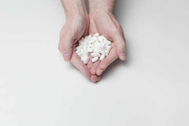 istock Two hands together hold a bunch of white pills on a white table. 1440766080