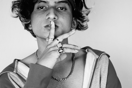 A grayscale shot of a cool Indian guy wearing a bandana and rings holding a finger on lips