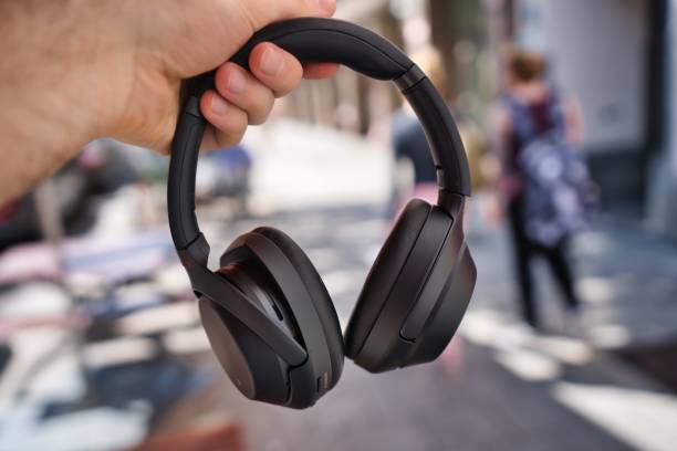 selective focus shot of a hand holding a pair of sony wh-1000xm3 headphones outdoors - sony imagens e fotografias de stock