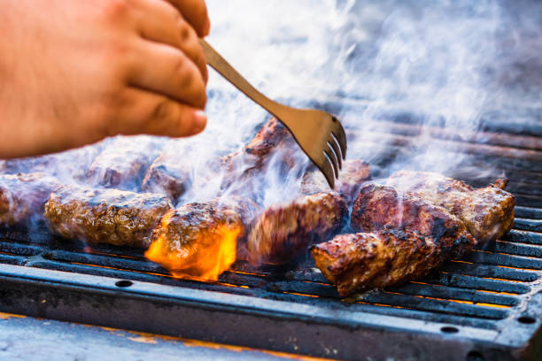 istock Closeup of a hand turning meat rolls with a fork called mici or mititei on a brazier 1440767933