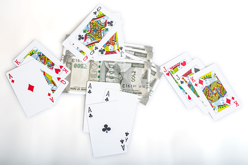 A top view of playing cards scattered around a pile of Indian rupee coins on a plain white background