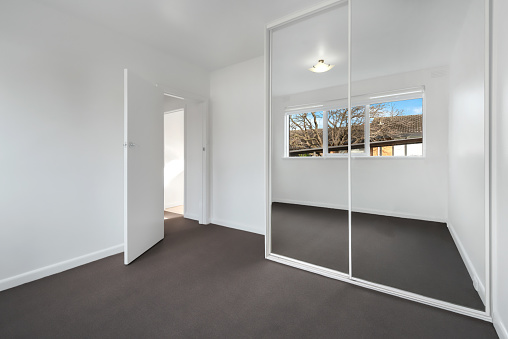 A corner of an empty new room with white walls and a wardrobe with mirror sliding doors