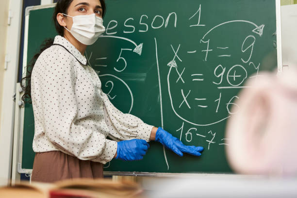 istock Female teacher wearing a facemask with latex gloves and explaining a math formula to the class 1440769992