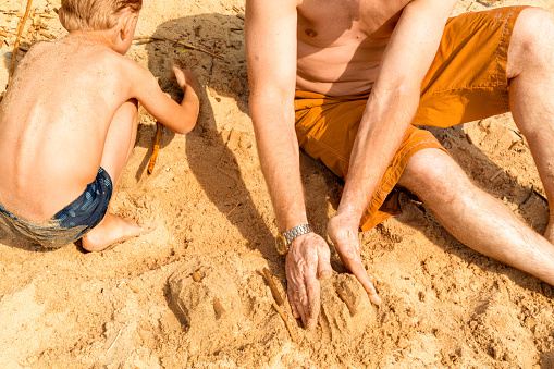 a father with vitiligo and his son play with sand on the beach on a hot summer day. Building castles. Without faces. The concept of a beach holiday.