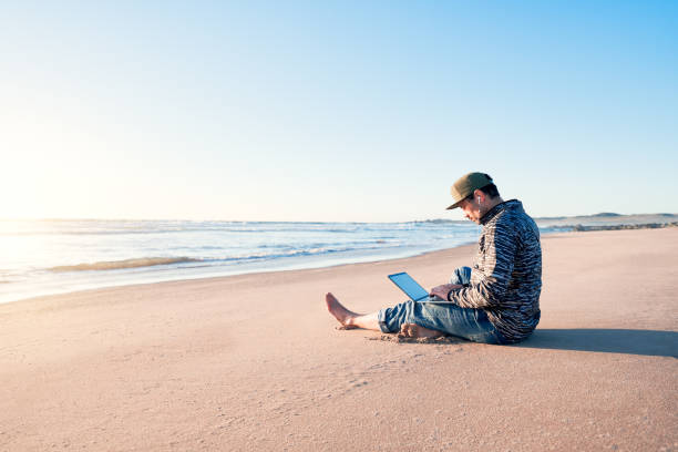 istock mature latin man sitting on the beach sand with his notebook working at sunset 1440771146