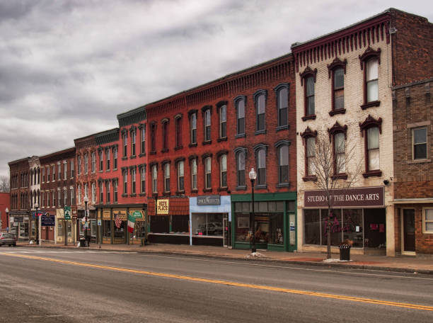 A photo of a typical small town main street in the United States of America. Features old brick buildings with specialty shops and restaurants. Decorated with spring flowers and American flags.